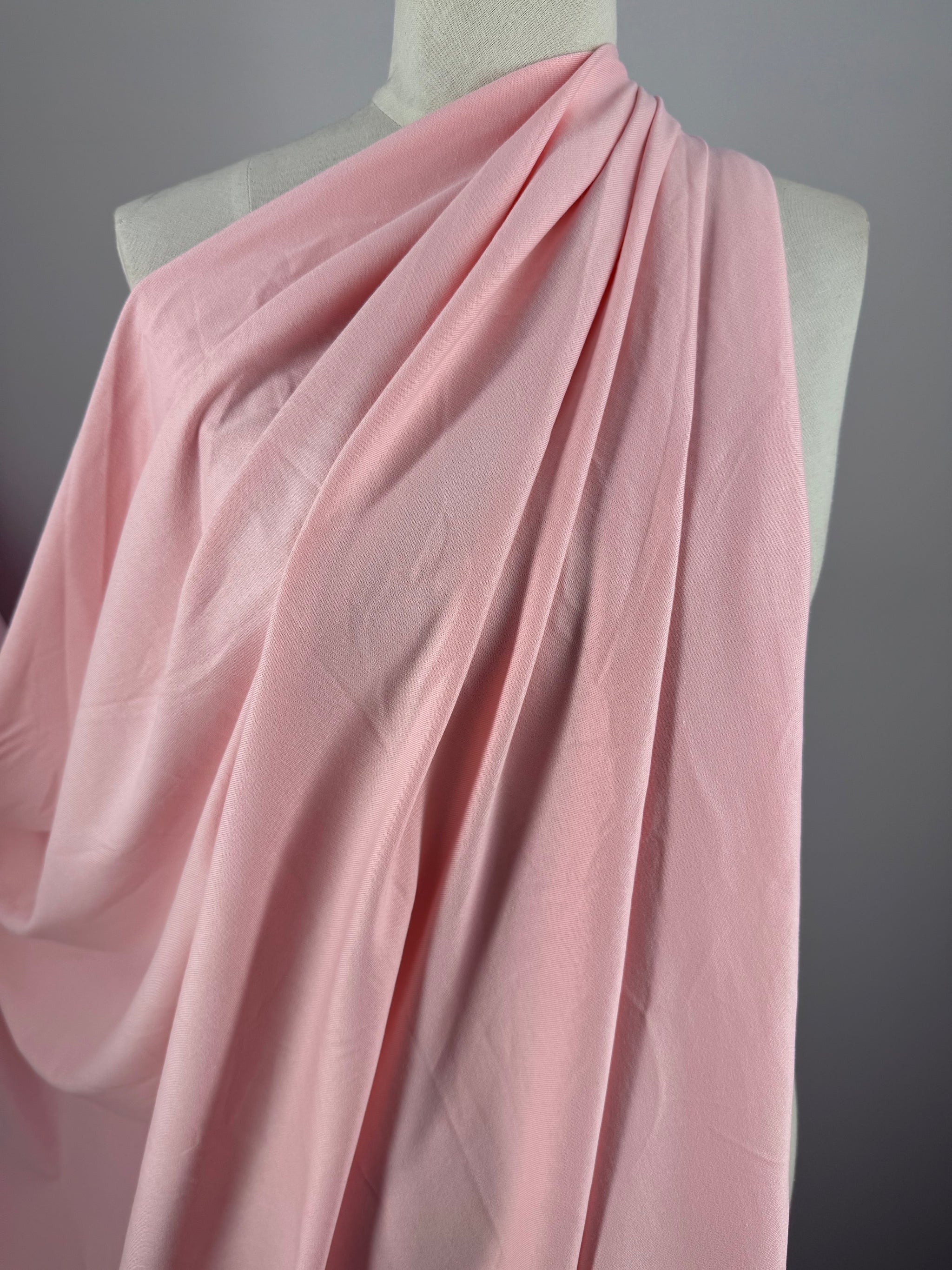 The Cotton Jersey - Tickled Pink fabric by Super Cheap Fabrics, measuring 170cm, elegantly drapes over a mannequin with gentle folds and a smooth texture. A neutral gray background accentuates the fabric's color and texture.
