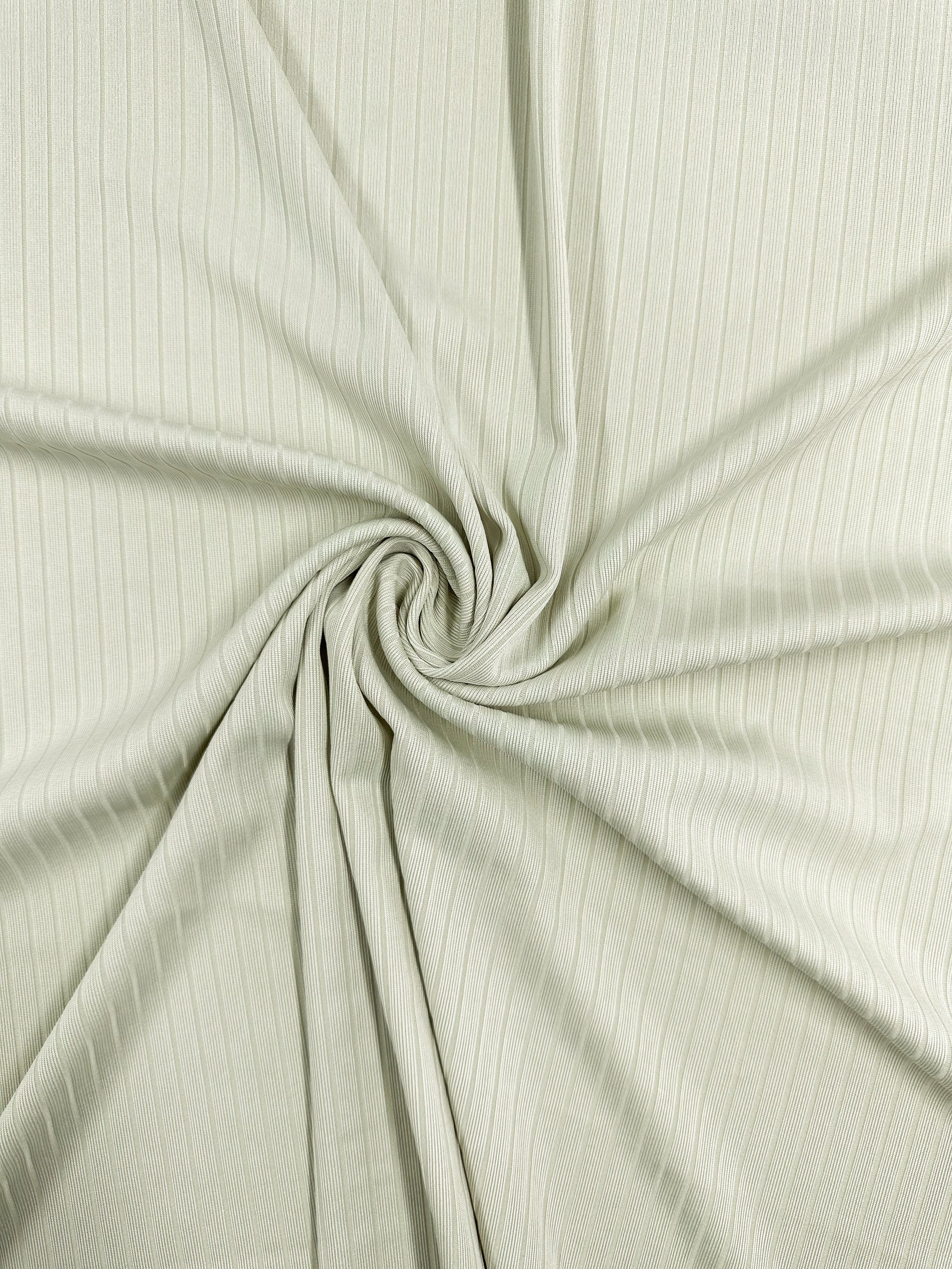 The Rib Knit - Celadon Tint by Super Cheap Fabrics features a close-up of pale green ribbed fabric gathered into a central swirl. This stretchy, medium-weight knit shows visible vertical lines for a subtle texture and pattern. Width: 168cm.