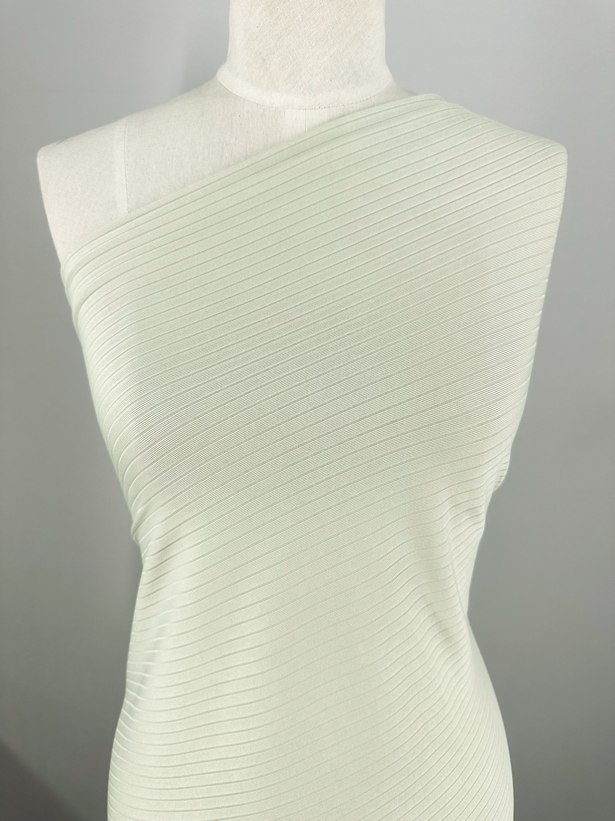 A celadon tint, ribbed, one-shoulder dress made from Super Cheap Fabrics' Rib Knit - Celadon Tint (168cm) is displayed on a mannequin. The medium-weight fabric's textured knit has a subtle sheen, highlighting its elegance and stretch against a plain background.