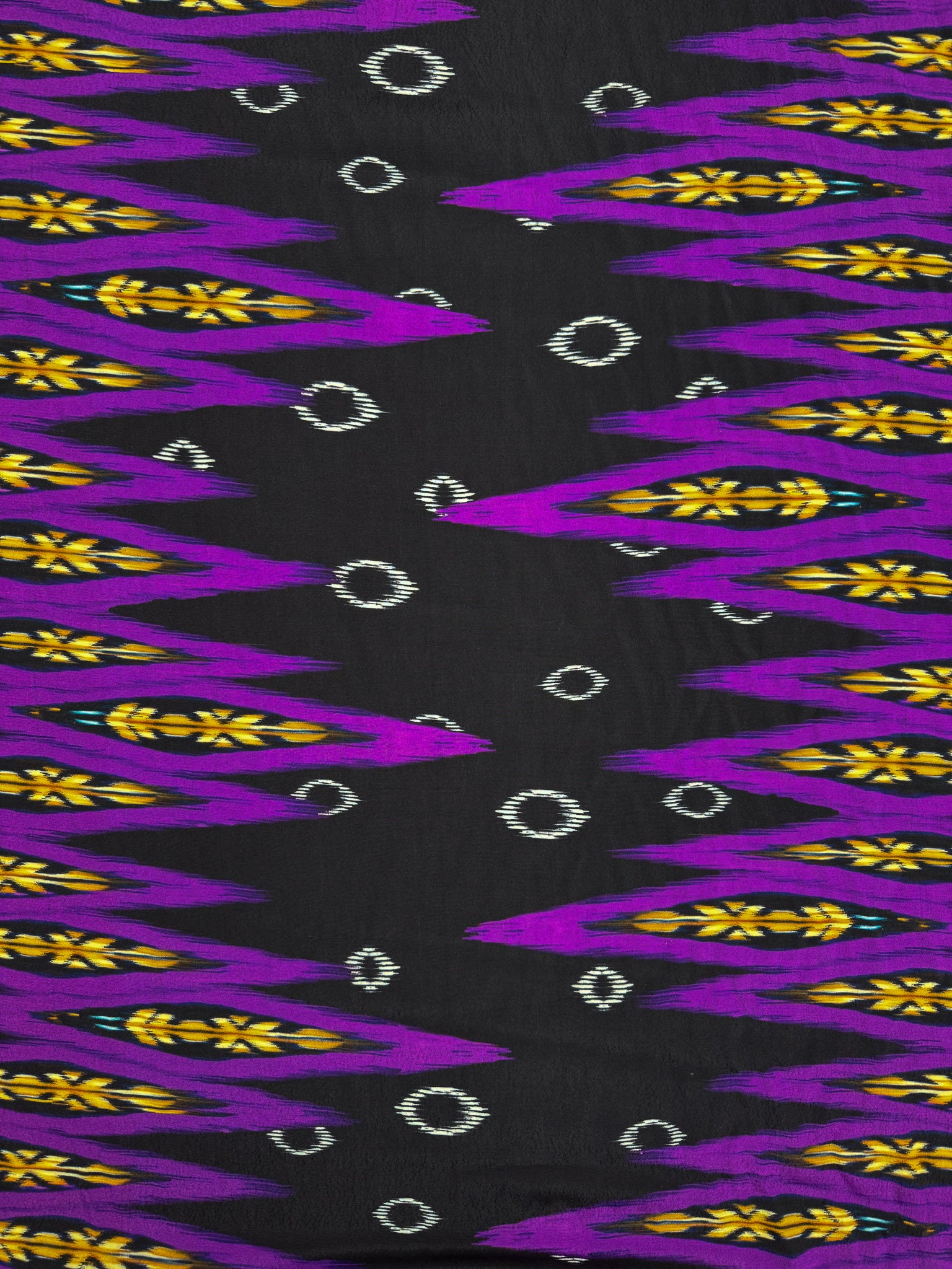 Super Cheap Fabrics’ Printed Viscose - Regal Ikat (145cm) features a black base with jagged purple and yellow zigzags plus small white diamonds arranged in rows.