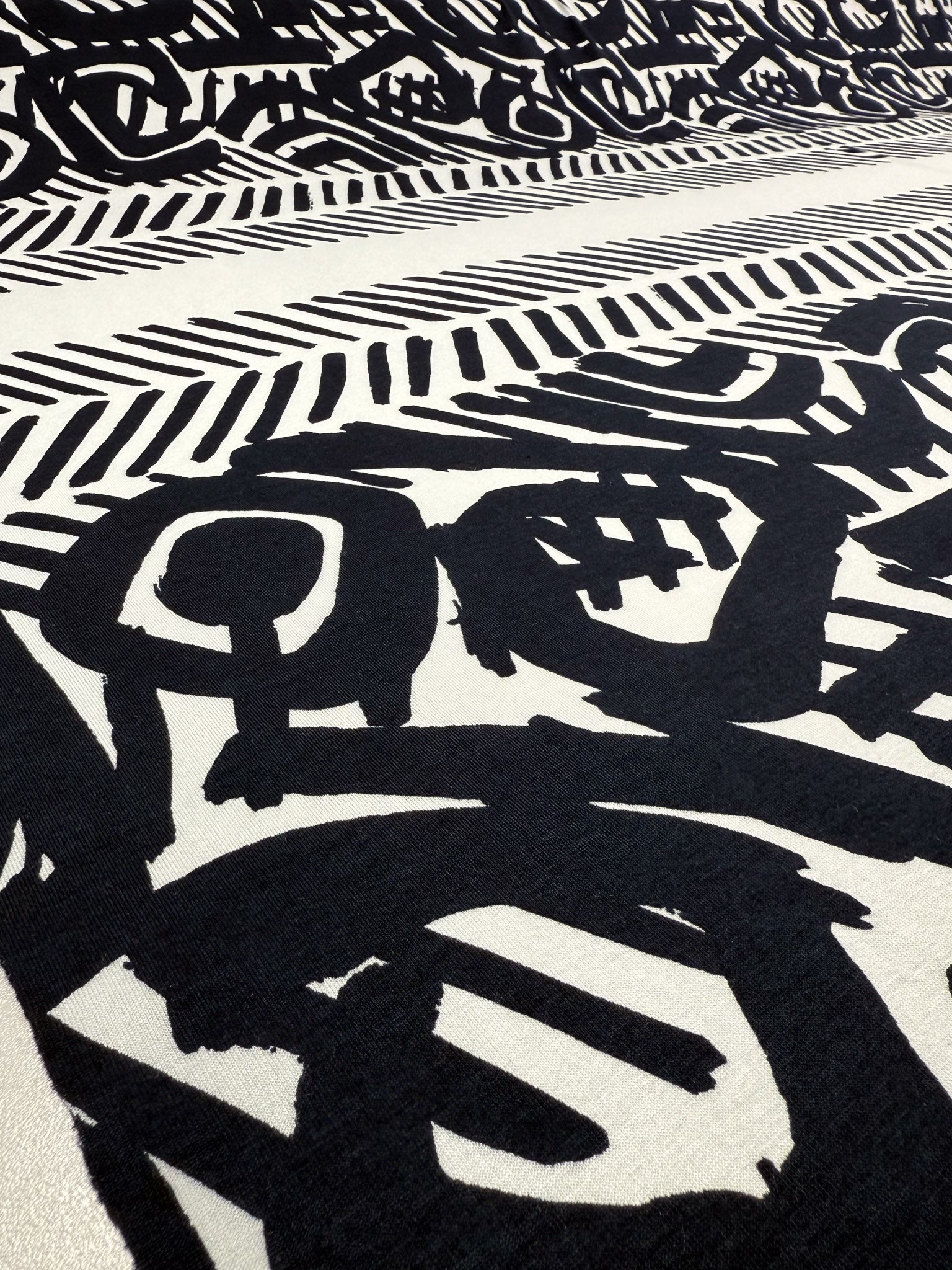 The Viscose Knit - Tribal Brushstroke by Super Cheap Fabrics features bold black abstract shapes and brushstroke patterns on cream, blending geometric lines with organic forms in a dynamic, breathable 142cm-wide summer fabric.