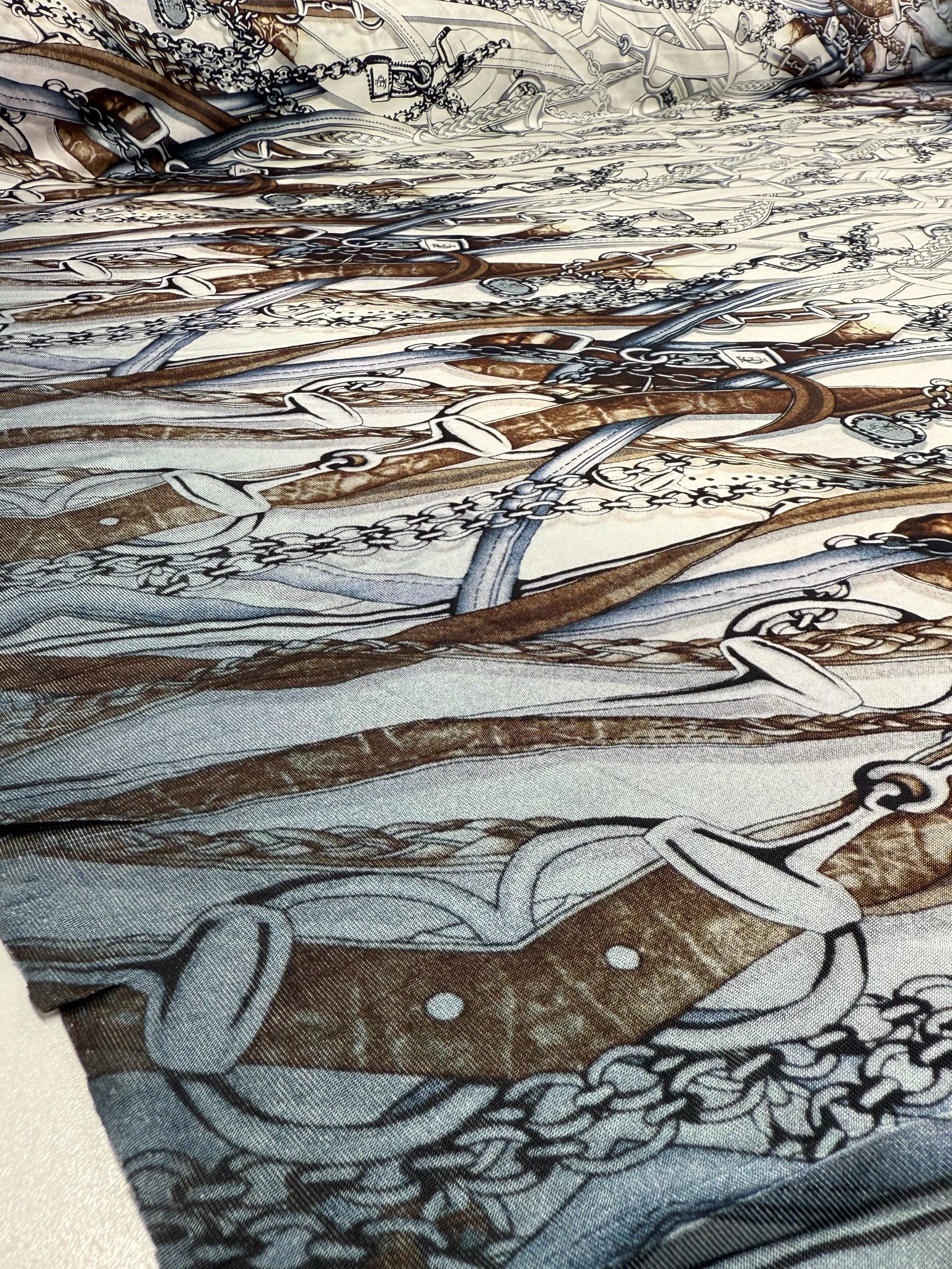 A close-up of Super Cheap Fabrics' Viscose Knit - Link (138cm) shows its intricate overlapping pattern of swords, ornate handles, and chains in brown, gray, and black on stretch fabric.