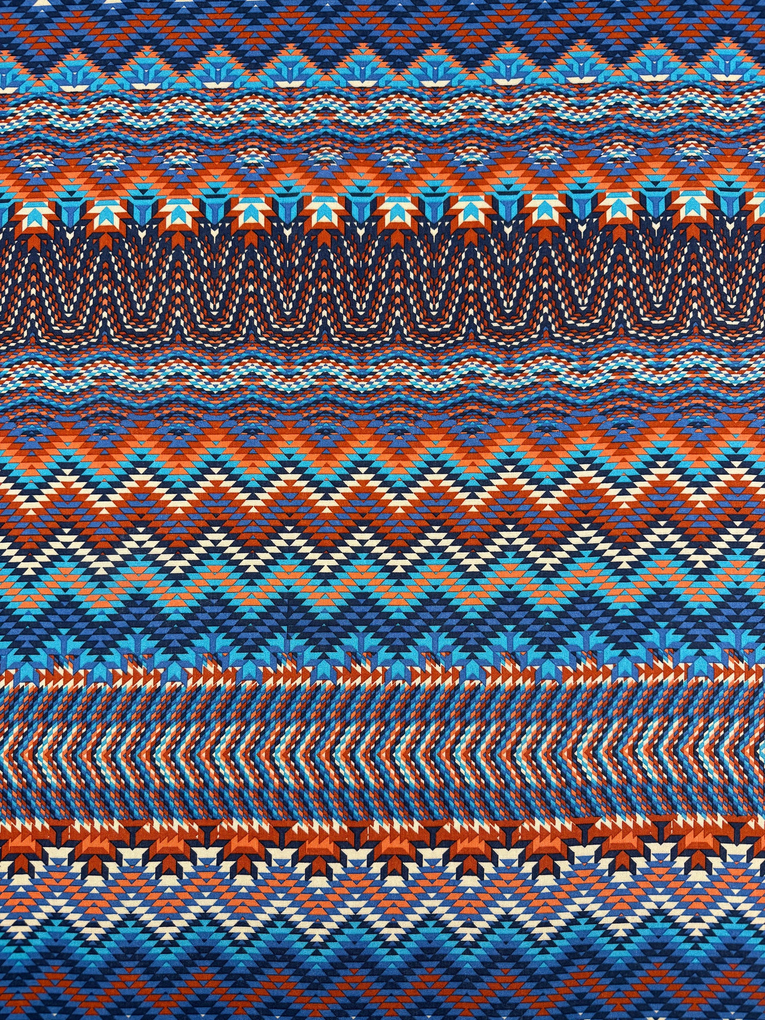 The Super Cheap Fabrics Printed Viscose - Zulu - 150cm features a vibrant, geometric zigzag pattern in blue, orange, red, and white, evoking traditional woven textiles with its symmetrical and sharp design.