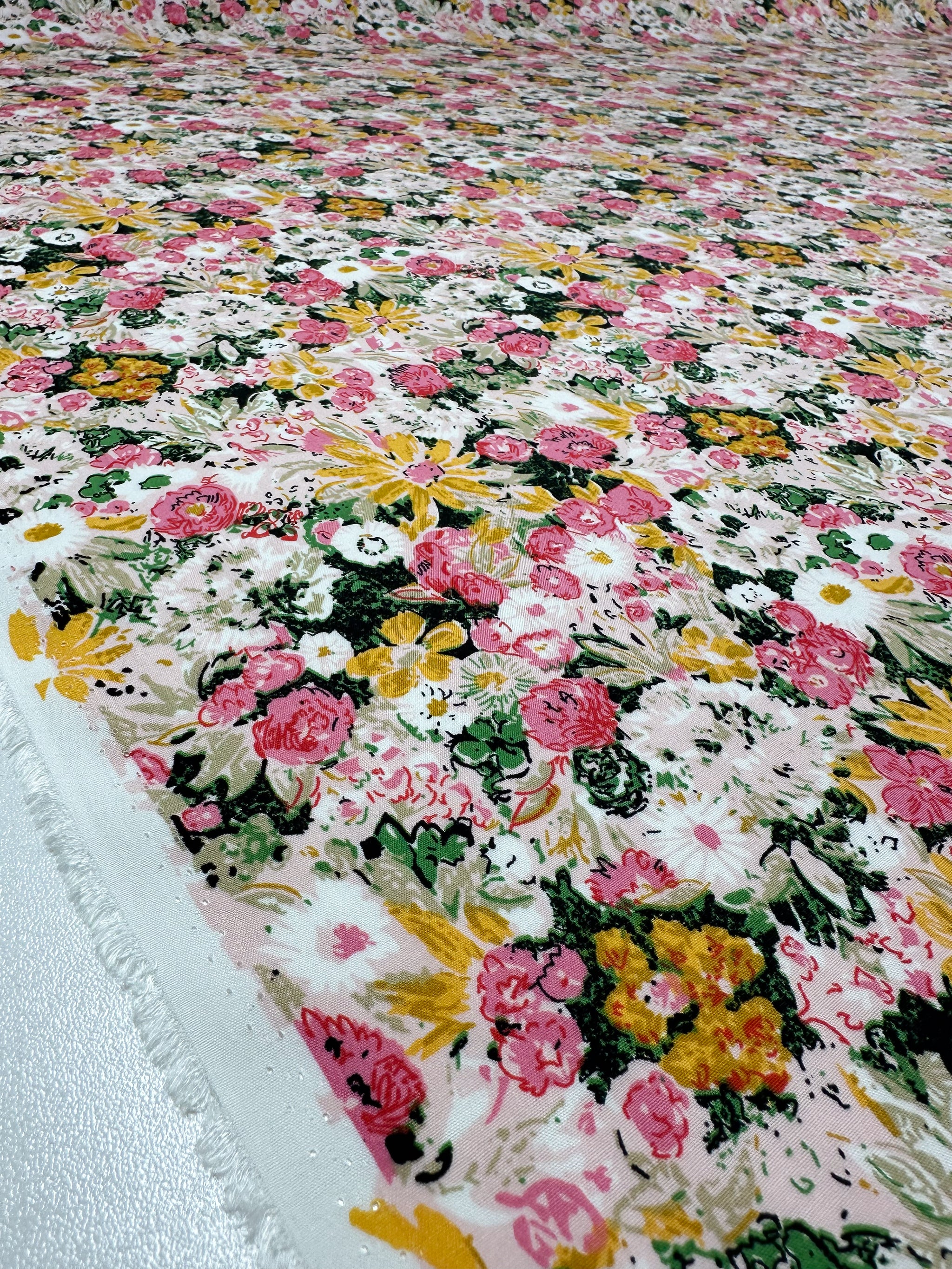 A close-up of Designer Rayon - Floral Garden (145cm) by Super Cheap Fabrics, showing its vibrant pink, yellow, and green floral print on white. The fabric lies flat to highlight its texture and colorful design.