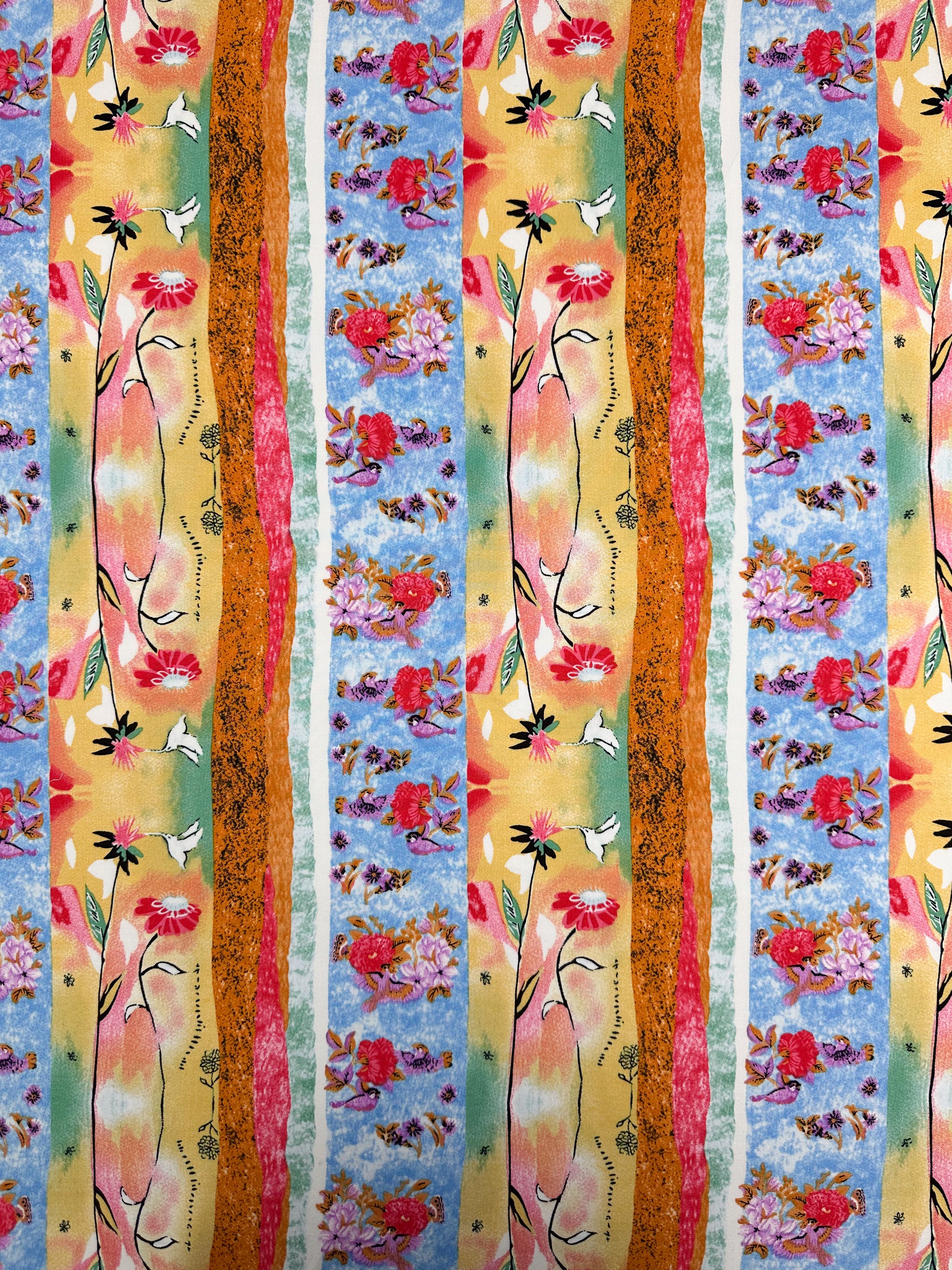 Designer Rayon - Wildframe - 145cm by Super Cheap Fabrics features vibrant vertical stripes with hand-drawn red flowers, green leaves, yellow shapes, and textured orange and blue bands, alternating with pink and purple floral clusters on blue.