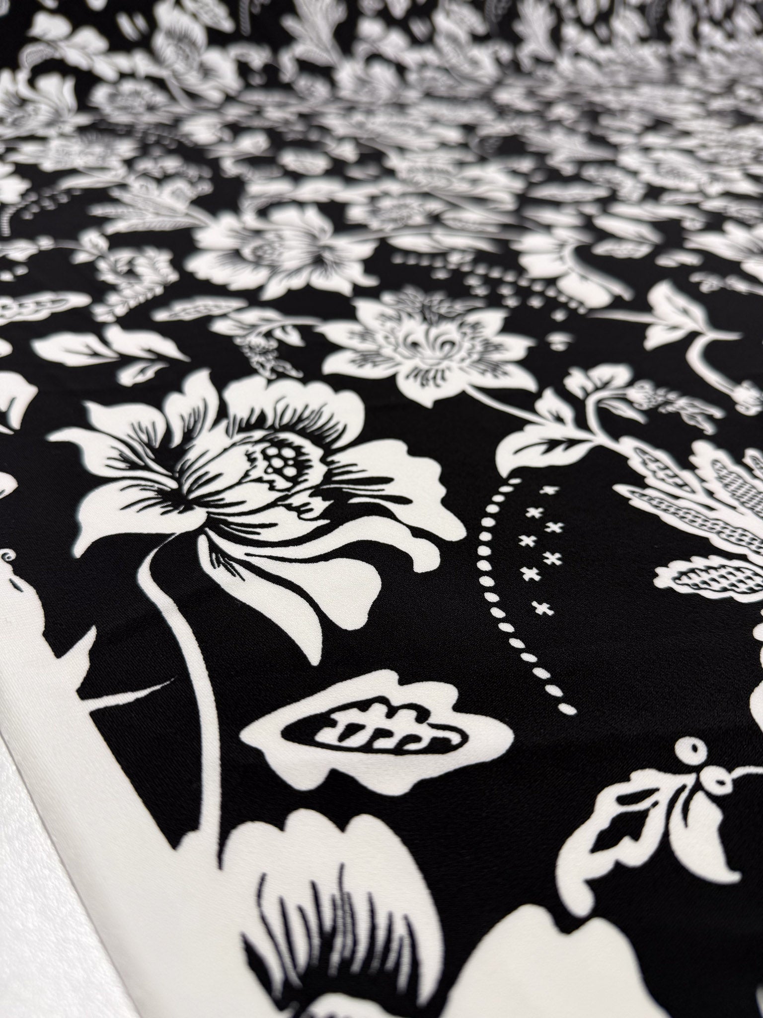 Super Cheap Fabrics' Printed Lycra - Monochrome Botanica (150cm) features a bold black and white floral pattern with leaves and decorative shapes, creating an intricate design on medium-weight lycra fabric.