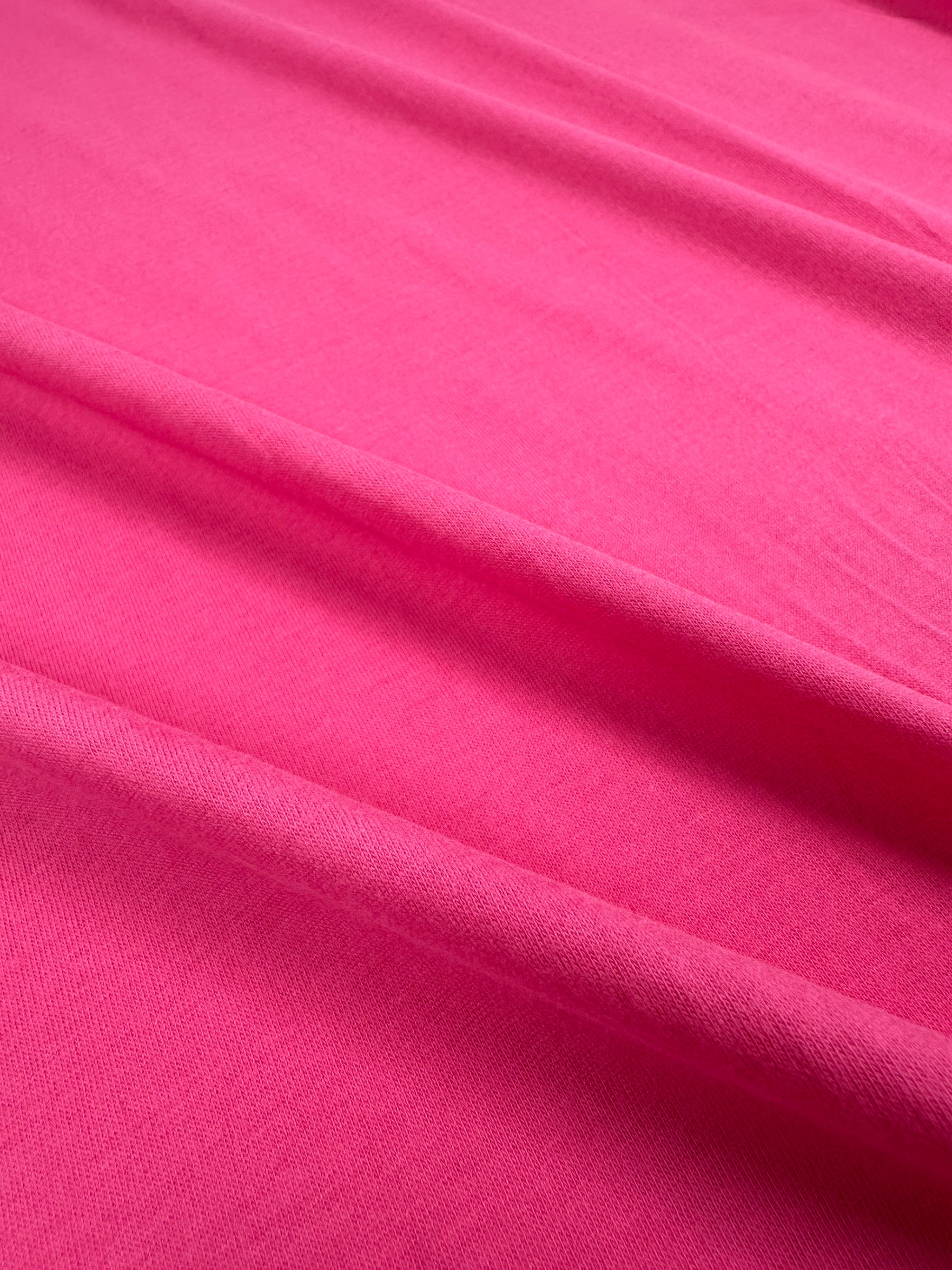 A close-up of the Cotton Jersey - Fandango Pink - 160cm by Super Cheap Fabrics, featuring gentle folds that highlight its soft texture and vibrant color.