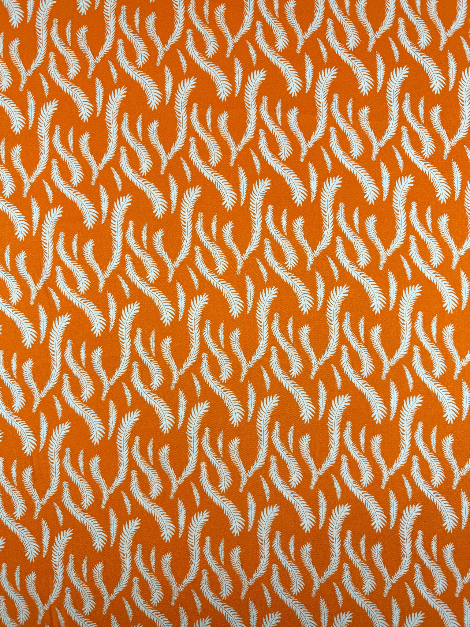 Super Cheap Fabrics’ Mercerised Rayon - Citrus Flow - 150cm features lightweight orange rayon with a repeating white fern motif, creating a dynamic, flowing effect and beautiful drape across the bright background.