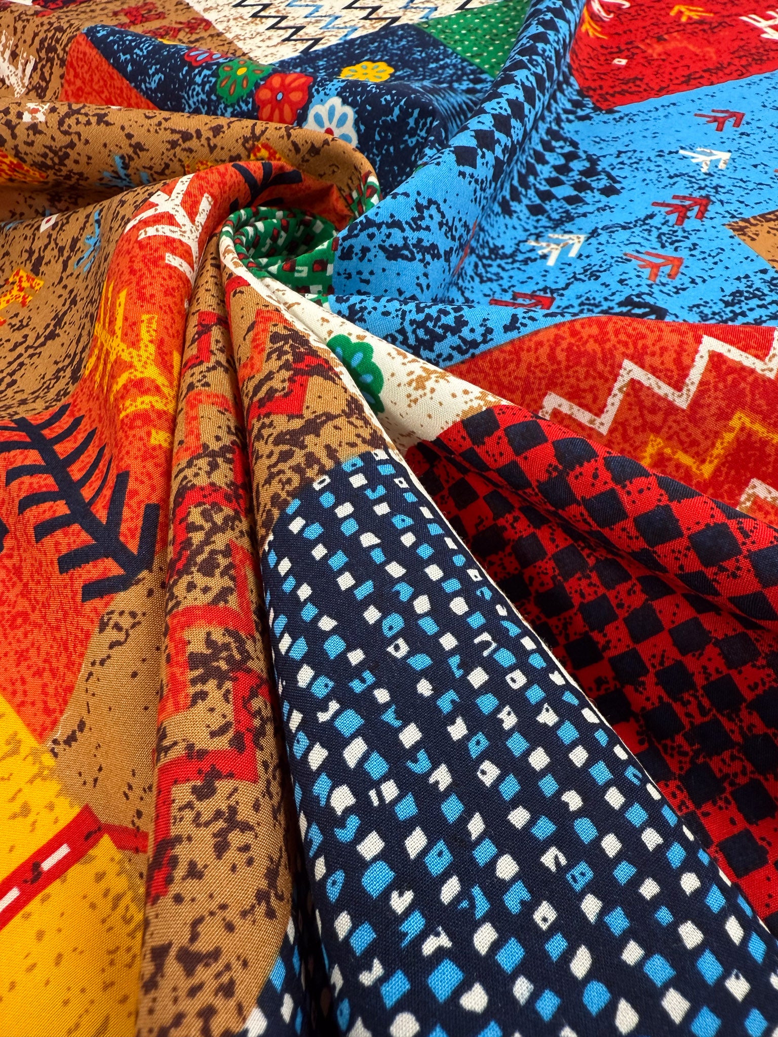 A close-up of Designer Rayon - Andes Patchwork by Super Cheap Fabrics shows colorful geometric and floral patterns in red, blue, brown, and yellow on 147cm fabric, artfully gathered to highlight its vivid texture.