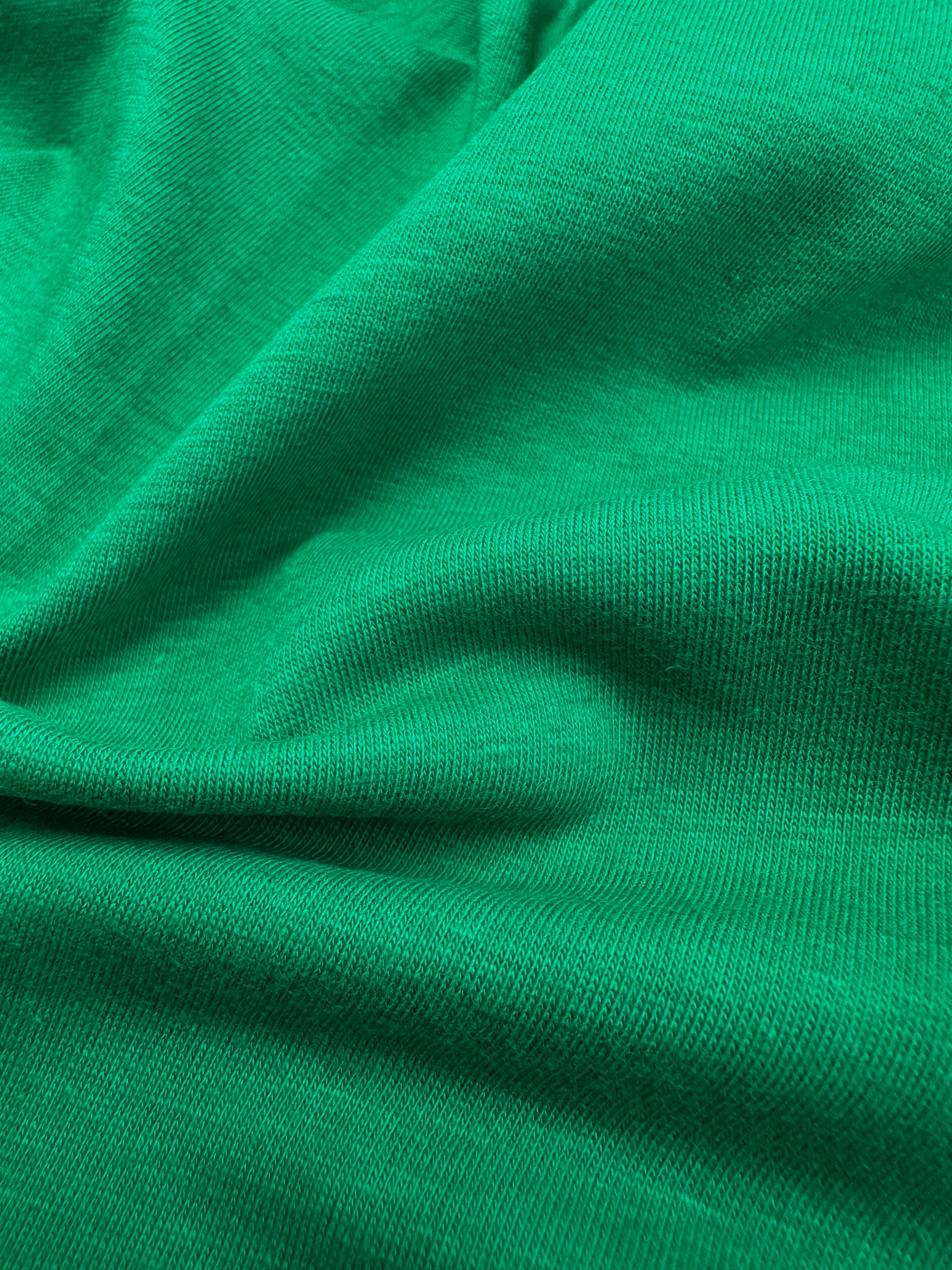 A close-up of Super Cheap Fabrics' Cotton Lycra in Green Tambourine, 160cm wide, reveals its vibrant textured surface. Gathered into soft folds, it showcases flexibility and drape perfect for bodycon dresses. Lighting highlights the weave beautifully.